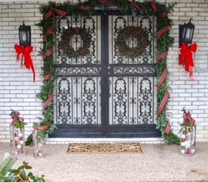 A traditional Christmas Front Door with plaid ribbon, garland, holly wreaths, and lanterns