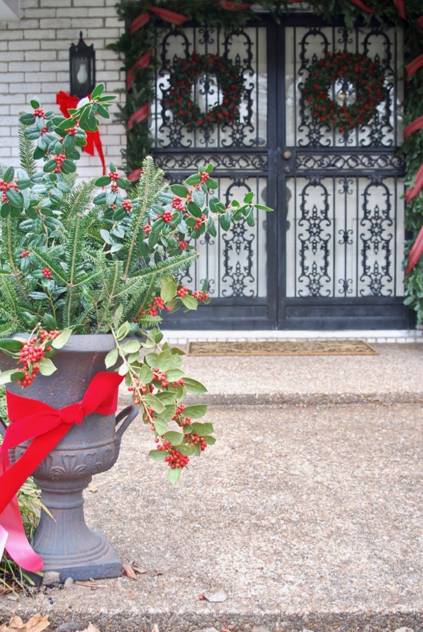 A traditional Christmas Front Door with plaid ribbon, garland, holly wreaths, and lanterns