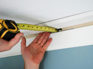 Measuring tape shows distance between wall and crown molding