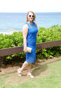 Wedding guest attire: blonde woman stands before ocean in blue crochet dress perfect for beach wedding.