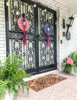 July 4th decorated front door with red, white, and blue DIY patriotic rosettes and star twinkle lights.