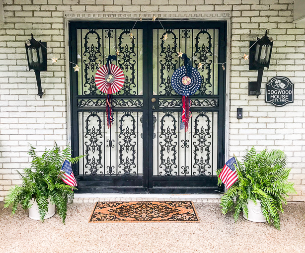 July 4th decorated front door with red, white, and blue DIY patriotic rosettes and star twinkle lights.