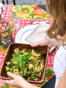 Woman carries pesto tortellini salad to summer al fresco dinner