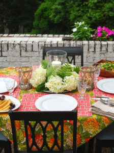 Hydrangea tablescape with coral placemats, hydrangea centerpiece with hurricane lantern, and colorful hydrangea tablecloth
