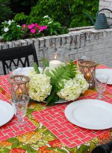 Hydrangea tablescape with coral placemats, hydrangea centerpiece with hurricane lantern, and colorful hydrangea tablecloth