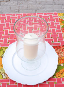 Step 2 to create hydrangea centerpiece with hurricane lantern shows white plate with candle and lantern