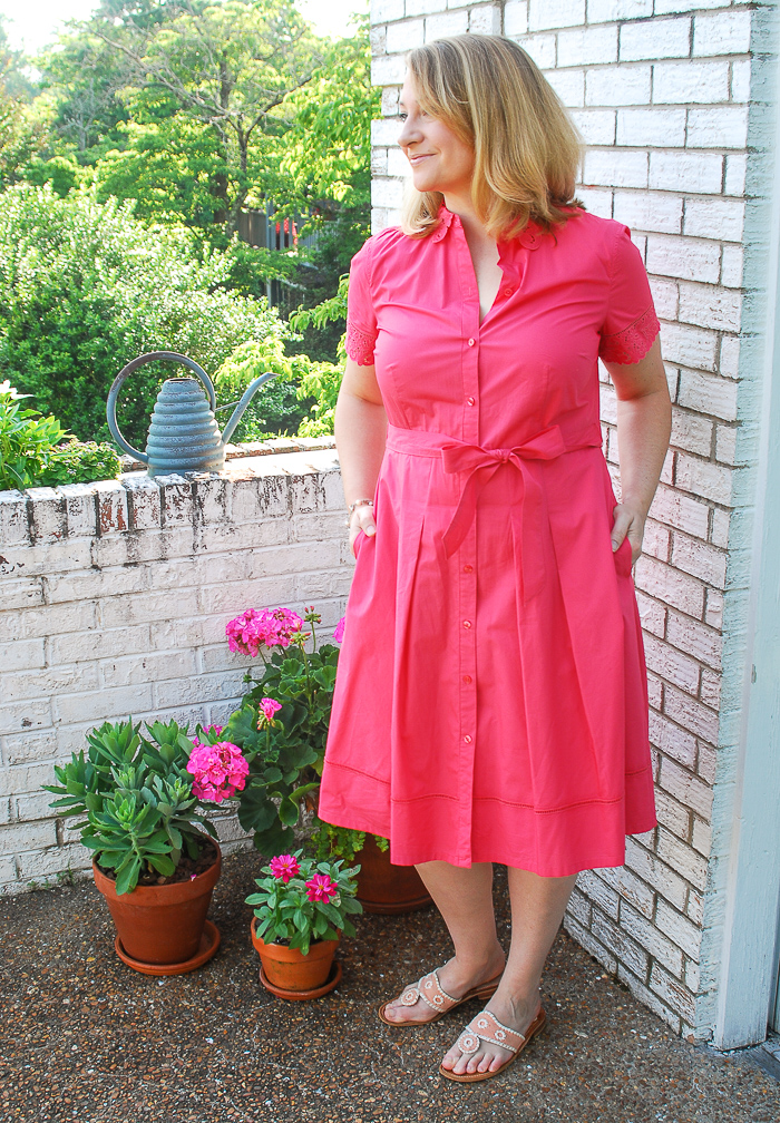 Blonde woman in pink shirtdress stands on balcony with flowers