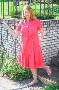 Blonde woman in front of gate wearing a pink shirtdress