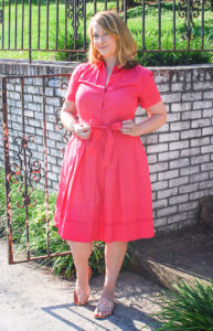 Blonde woman in front of gate wearing a pink shirtdress