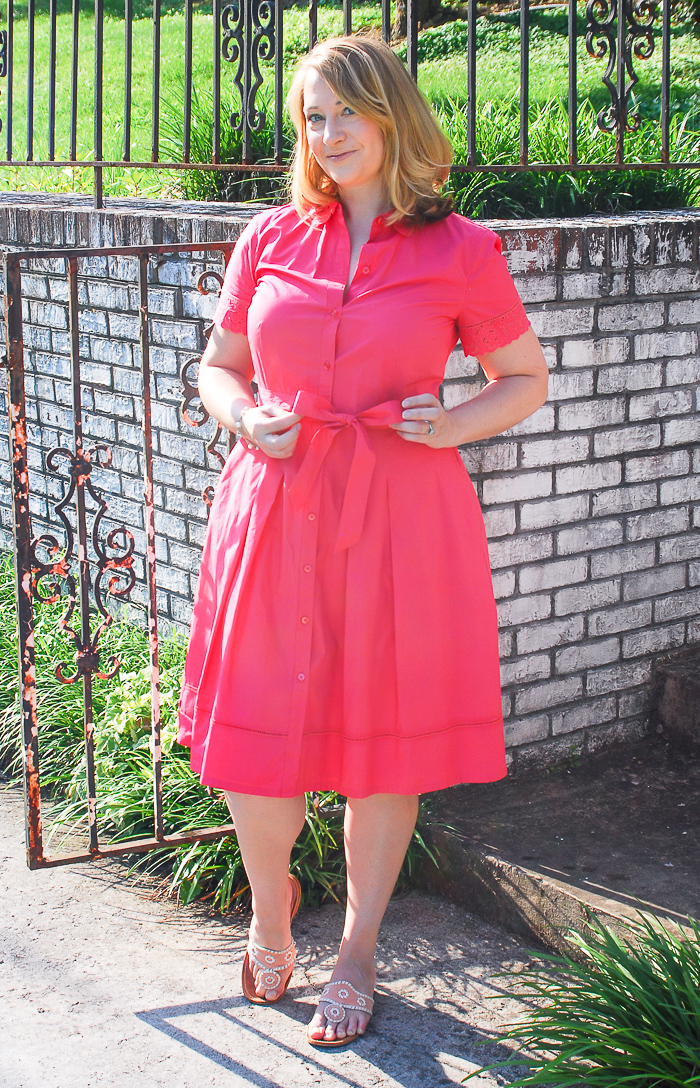 Blonde woman in front of gate wearing a pink shirtdress
