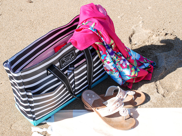 Summer essentials for the beach tossed in beach bag sitting in the sand