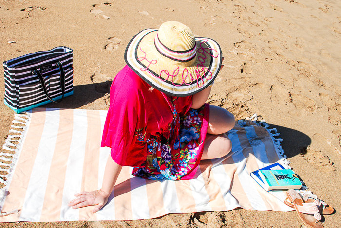Woman on striped beach towel in floral pink coverup and sunhat - summer beach essentials