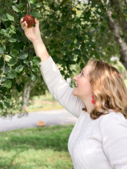 Partake in autumn adventures with this fall bucket list - Blonde woman reaching up to pick an apple.