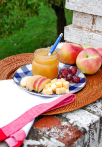 Jar of cinnamon ginger applesauce with grapes and cheese on gingham plate