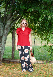 Blonde woman stands under tree in fall transition outfit of garnet blouse and palazzo pants