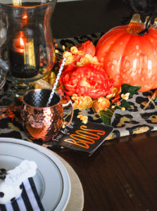 Glam Halloween table set with copper mugs, leopard print runner, dramatic orange and yellow florals, glass pumpkins, and spooky crows.
