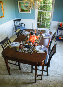 Glam Halloween table set with copper mugs, leopard print runner, dramatic orange and yellow florals, glass pumpkins, and spooky crows.