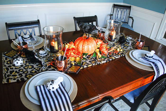 Glam Halloween table set with copper mugs, leopard print runner, dramatic orange and yellow florals, glass pumpkins, and spooky crows.