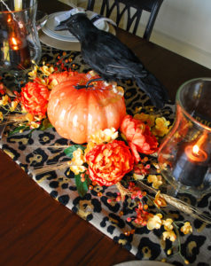 Glam Halloween table set with copper mugs, leopard print runner, dramatic orange and yellow florals, glass pumpkins, and spooky crows.