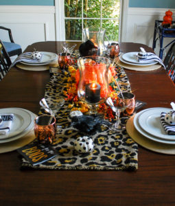 Glam Halloween table set with copper mugs, leopard print runner, dramatic orange and yellow florals, glass pumpkins, and spooky crows.