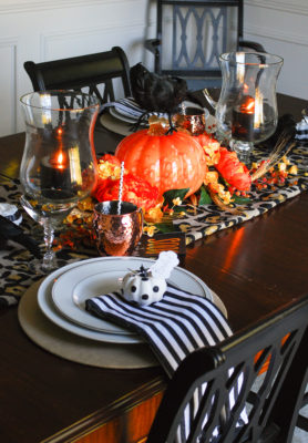 Glam Halloween table set with copper mugs, leopard print runner, dramatic orange and yellow florals, glass pumpkins, and spooky crows.