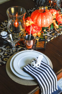 Glam Halloween table set with copper mugs, leopard print runner, dramatic orange and yellow florals, glass pumpkins, and spooky crows.