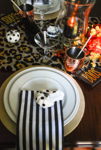 Glam Halloween table set with copper mugs, leopard print runner, dramatic orange and yellow florals, glass pumpkins, and spooky crows.