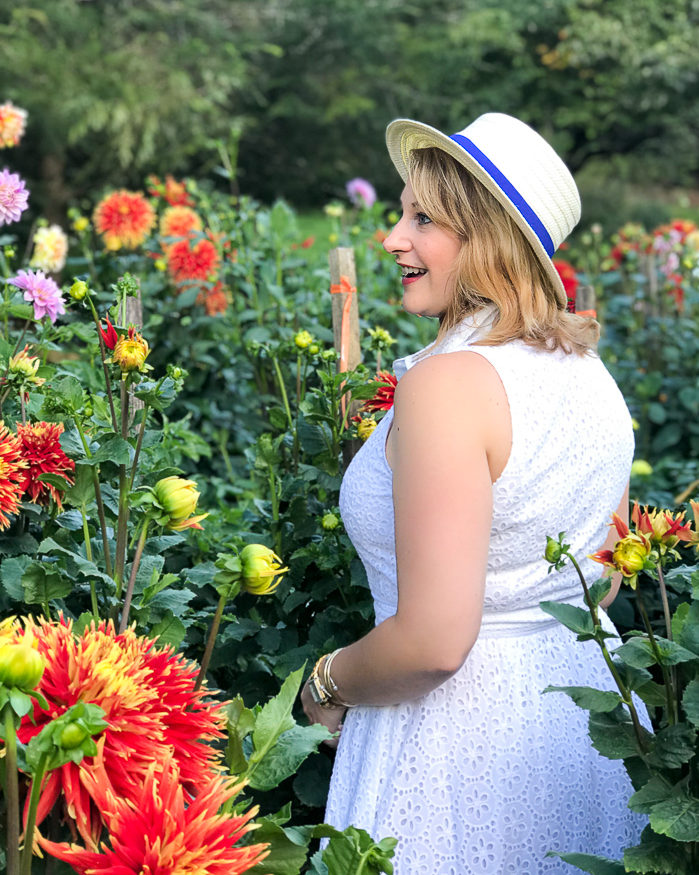 Thoughts on a gracious disposition - woman in white dress and hat stands in field of dahlias