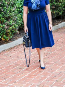 Blonde woman in navy work dress from gal meets glam with blue scarf tied in bow.