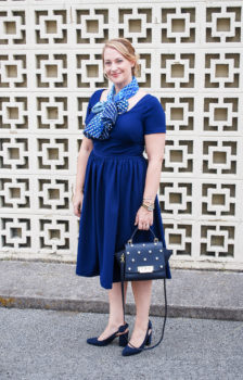 Blonde woman in navy work dress from gal meets glam with blue scarf tied in bow.