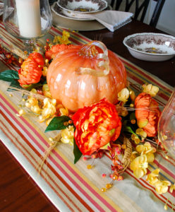 Autumn tablescape with budget friendly pumpkin centerpiece, Mason's ironstone, striped table runner, glass hurricanes, fall florals, and copper mugs.