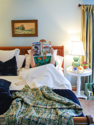 Woman reading magazine in comfy bed made with best bed sheets from California Design Den