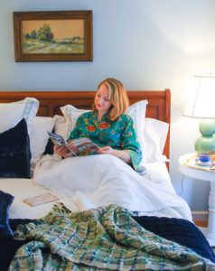 Woman reading magazine in comfy bed made with best bed sheets from California Design Den