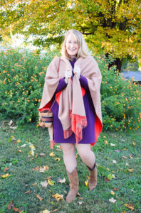 Blonde woman in the perfect purple dress from Joules poses in front of tree with yellow leaves