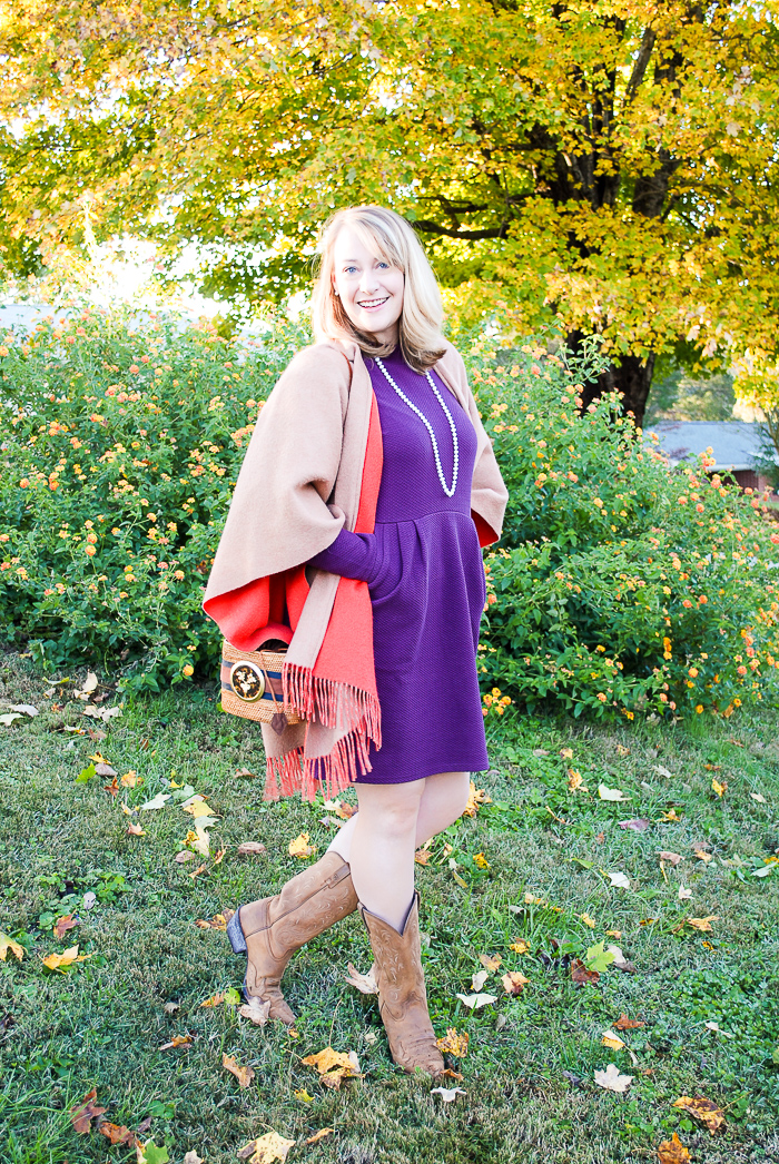 Blonde woman in the perfect purple dress from Joules and merino wrap poses in front of tree with yellow leaves