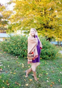 Blonde woman in the perfect purple dress from Joules and merino wrap poses in front of tree with yellow leaves