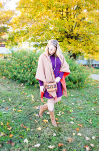 Blonde woman in the perfect purple dress from Joules and merino wrap poses in front of tree with yellow leaves