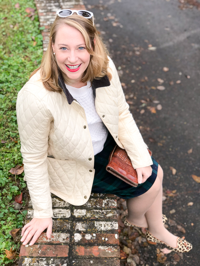 Casual holiday look with black watch skirt, Barbour coat, cable knit sweater, leopard print loafers, and leather clutch.