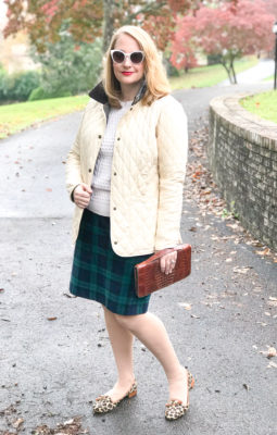 Casual holiday look with black watch skirt, Barbour coat, cable knit sweater, leopard print loafers, and leather clutch.