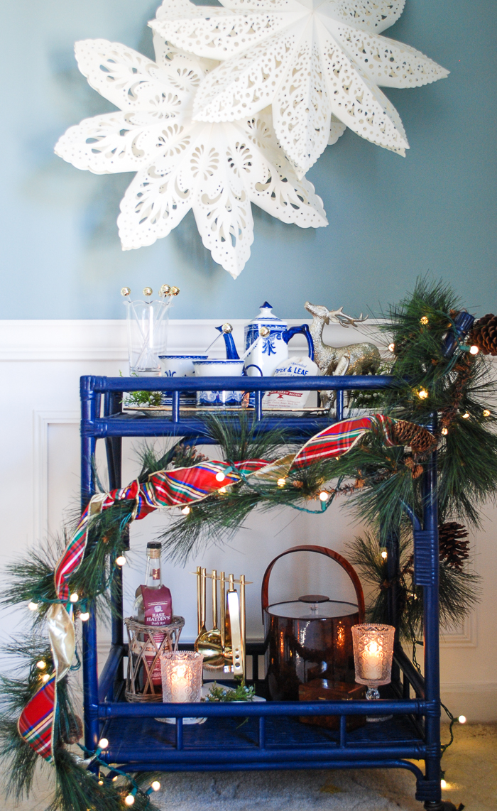 Lemon berry hot toddy on blue rattan bar cart decorated for the holidays with pine and plaid.