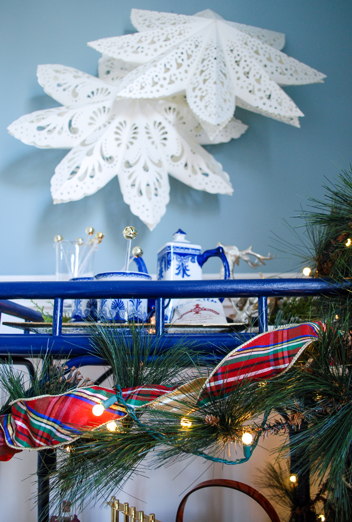 Lemon berry hot toddy on blue rattan bar cart decorated for the holidays with pine and plaid.