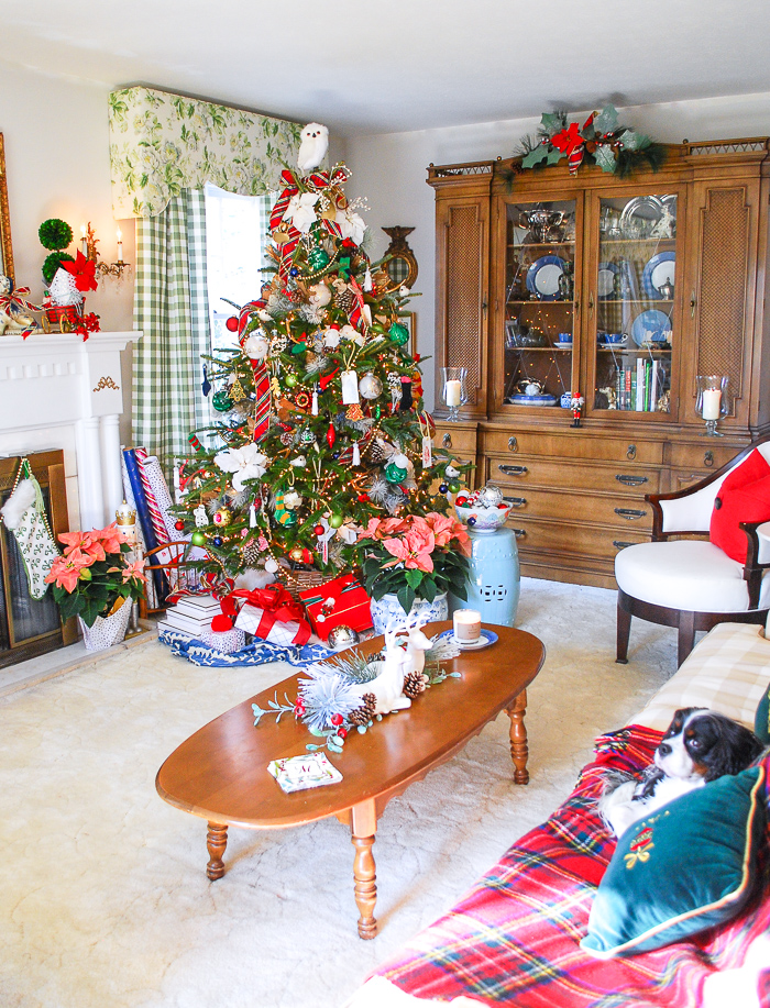 Preppy & plaid Christmas tree in front of window and bookcase in traditional living room trimmed with red and green plaid ribbon, poinsettia, vintage ornaments, and gold.