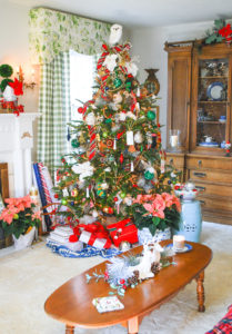 Preppy & plaid Christmas tree in front of window and bookcase in traditional living room trimmed with red and green plaid ribbon, poinsettia, vintage ornaments, and gold.