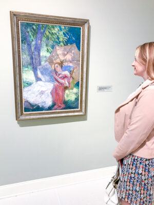 Blond woman gazes at impressionist painting of woman reading by Catherine Wiley