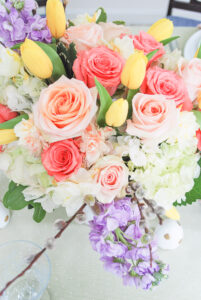 Vibrant floral centerpiece with pink roses, yellow tulips, hydrangea, pussy willow, and purple gillyflowers for a pastel Easter brunch table