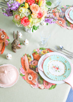 An Easter brunch table in pretty pastels with bunny placemats, antique china, etched stemware, and vibrant floral centerpiece