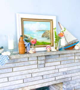 Get in a summer state of mind with this nautical summer mantel with vintage decor, featuring a sailboat, coral, seashells, and wicker.