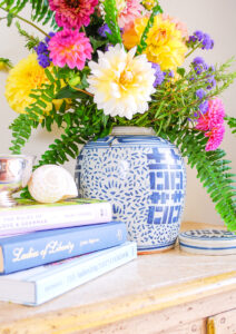 Blue and white ginger jar floral arrangement with dahlias and fern on antique sideboard with books