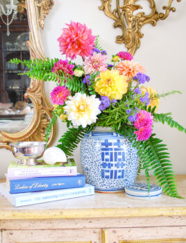 Blue and white ginger jar floral arrangement with dahlias and fern on antique sideboard with books