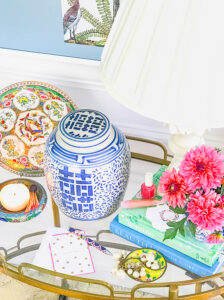 Top view of blue and white ginger jar with pink dahlias, marble lamp, rose medallion plate, and candle.